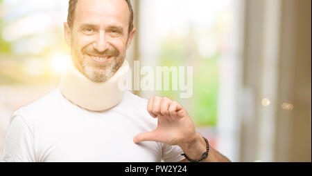 Injured senior man using a neck brace proud, excited and arrogant, pointing with victory face Stock Photo