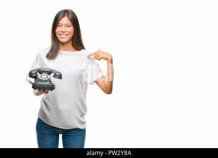 Young asian woman holding vintagera telephone over isolated background with surprise face pointing finger to himself Stock Photo