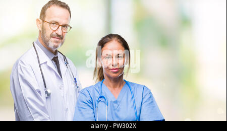Middle age hispanic doctors partners couple wearing medical uniform over isolated background with serious expression on face. Simple and natural looki Stock Photo