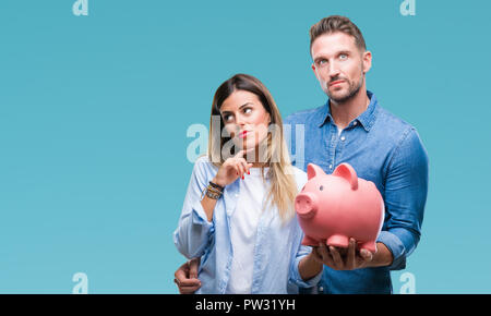 Young couple in love holding piggy bank over isolated background serious face thinking about question, very confused idea Stock Photo