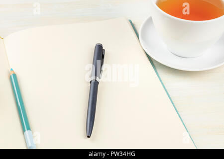 A photo of an open journal with a pen, a pencil, and a cup of tea on a teal blue background Stock Photo