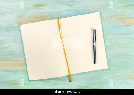 A top shot of an open journal with a pen on a teal blue background with a place for text Stock Photo