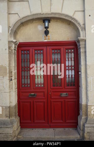 A bright red wooden door on a limestone wall in a country town in France Stock Photo