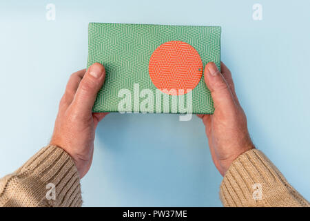 Hands giving green Christmas present gift box on blue background Stock Photo