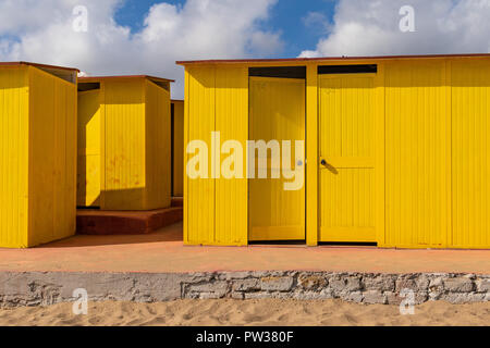 Beautiful yellow Bathing houses on the sandy beach. Empty shelters on a sunny but moody day. Seaside architecture, colored paint, maze-like labyrint.