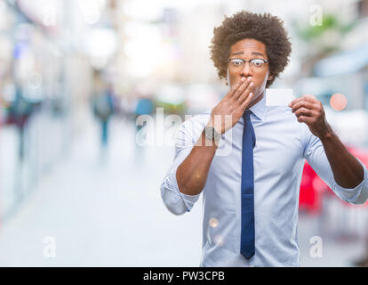 Afro american man holding visit card over isolated background cover mouth with hand shocked with shame for mistake, expression of fear, scared in sile Stock Photo