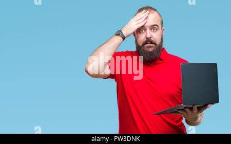 Young caucasian man using computer laptop over isolated background stressed with hand on head, shocked with shame and surprise face, angry and frustra Stock Photo