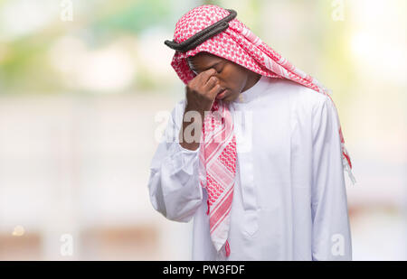 Young arabic african man wearing traditional keffiyeh over isolated background tired rubbing nose and eyes feeling fatigue and headache. Stress and fr Stock Photo