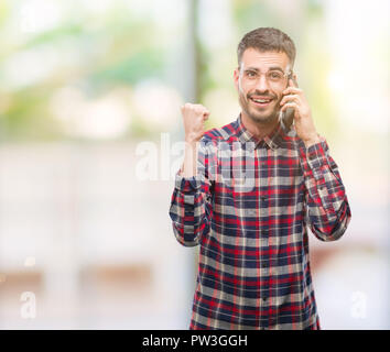 Young hipster adult man talking on the phone screaming proud and celebrating victory and success very excited, cheering emotion Stock Photo