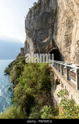 scenic road and tunnel under vertical rock walls on lakeside, shot in bright fall light near Riva del Garda, Trento, Italy Stock Photo