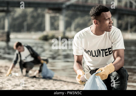 Handsome dark-haired student being socially active while cleaning the beach Stock Photo
