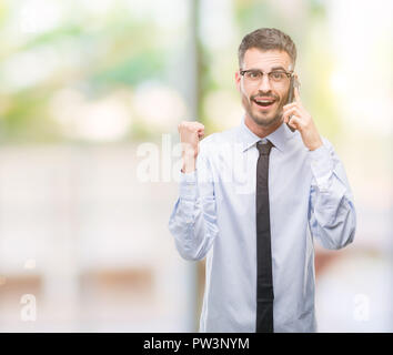 Young business adult man talking on the phone screaming proud and celebrating victory and success very excited, cheering emotion Stock Photo