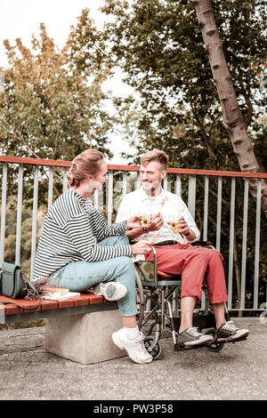 Relaxed woman sitting with disabled man and eating healthy food Stock Photo