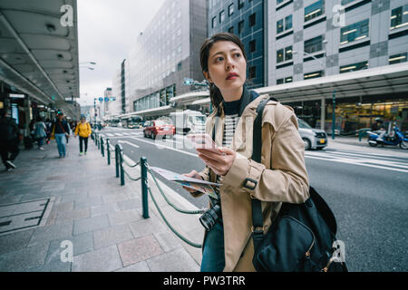 elegant female traveler standing on the street and using smartphone to check the route of her plan. backpacker using online map app. busy Japanese cit Stock Photo