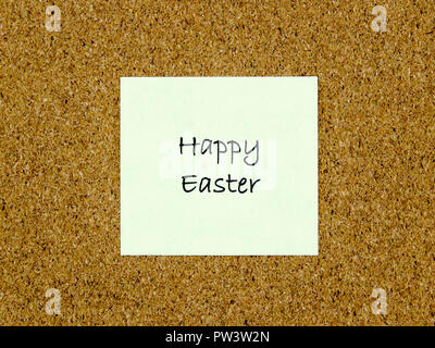 A yellow sticky note with happy easter written on it on a cork board background Stock Photo