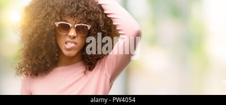 African american woman wearing pink sunglasses confuse and wonder about question. Uncertain with doubt, thinking with hand on head. Pensive concept. Stock Photo