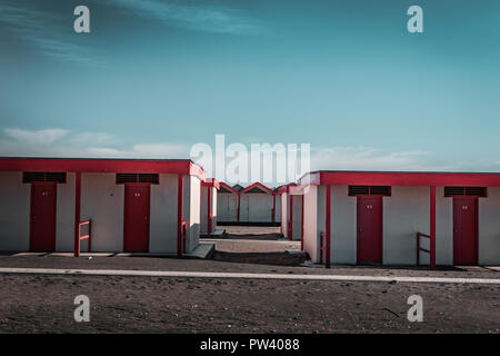 Beautiful Red Bathing houses on sandy beach. Empty shelters on a sunny but moody day. Seaside architecture, colored paint, maze like labyrinth. Alone.