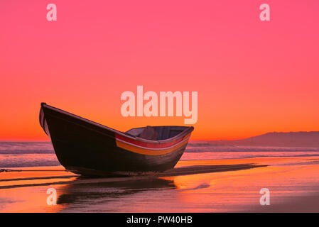 A picturesque wooden boat at a golden beach in Lisbon at sunset Stock Photo