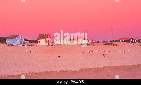 Colorful beach houses on the Costa da Caparica Beach in Lisbon, at sunset with an orange sky and golden sandy beach view Stock Photo