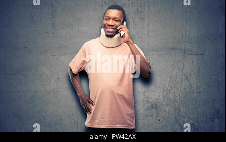 Injured african black man wearing neck brace happy talking using a smartphone mobile phone Stock Photo