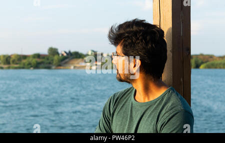 Profile picture of indian man wearing eyeglasses or spectacles looking at water and contemplating with natural lake background Stock Photo