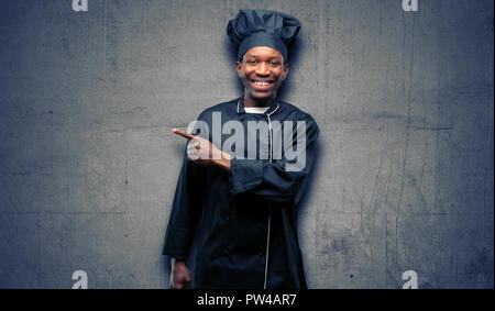 Young black cook wearing chef hat pointing away side with finger Stock Photo