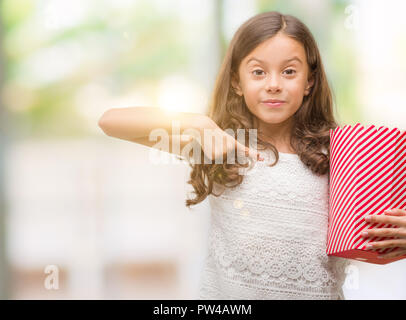 Brunette hispanic girl eating popcorn with surprise face pointing finger to himself Stock Photo
