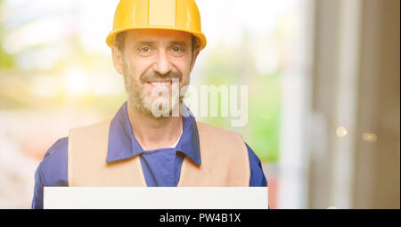 Senior engineer man, construction worker holding blank advertising banner, good poster for ad, offer or announcement, big paper billboard Stock Photo