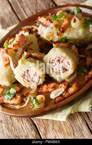 Baltic Cepelinai potato dumplings with meat filling served with bacon and fried onions close-up on table. vertical Stock Photo