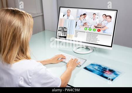 Female Dentist Video Conferencing With Her Colleagues On Computer In Clinic Stock Photo