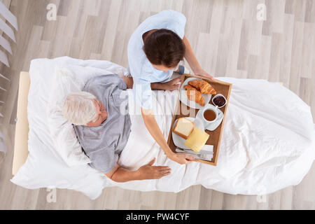 Overhead View Of Female Nurse Serving Food To Senior Male Patient In Clinic