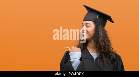 Young hispanic woman wearing graduation uniform pointing and showing with thumb up to the side with happy face smiling Stock Photo