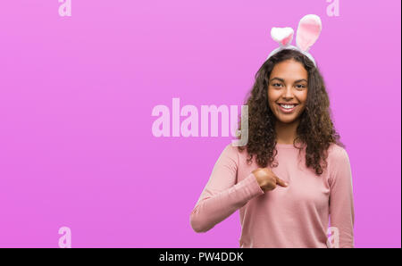 Young hispanic woman wearing easter bunny ears with surprise face pointing finger to himself Stock Photo
