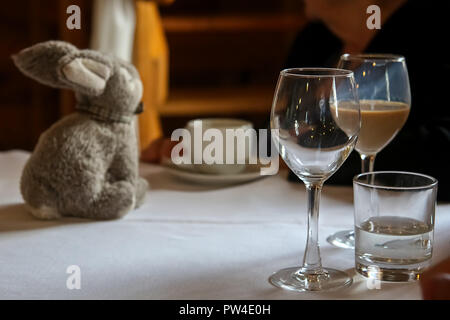 Glass with Irish creme liqueur, empty glass, glass with water, cofee cup and rabbit on the table. Stock Photo