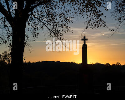 War memorial cross silhouetted against a sunset sky the the Castle Grounds at Knaresborough North Yorkshire England Stock Photo