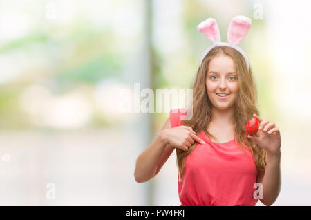 Young blonde woman wearing easter bunny ears with surprise face pointing finger to himself Stock Photo