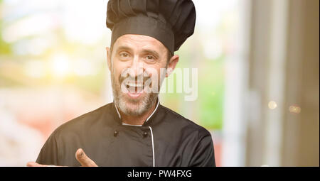 Senior cook man, wearing chef hat holding something in empty hand Stock Photo