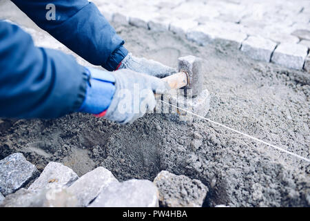 construction worker placing stone tiles for pavement, terrace. Worker placing granite cobblestone pavement at terrace Stock Photo