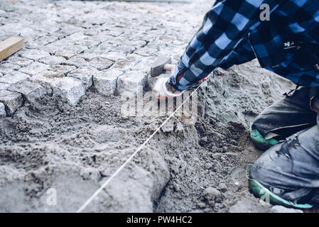industrial worker installing pavement rocks, cobblestone blocks on road pavement Stock Photo