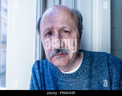 Old senior man looking throughout the window feeling confused and depressed alone at home in Aging Retirement Widower Dementia and Alzheimer concept. Stock Photo