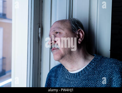 Senior man in his 60s feeling desperate sad looking throughout the balcony worried depressed thoughtful and lonely at home in Aging Depression Mental  Stock Photo