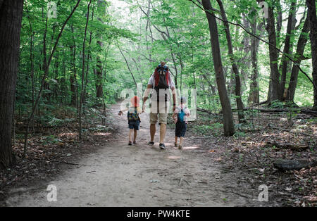 Rear view of father holding children's hands while walking on road in forest Stock Photo