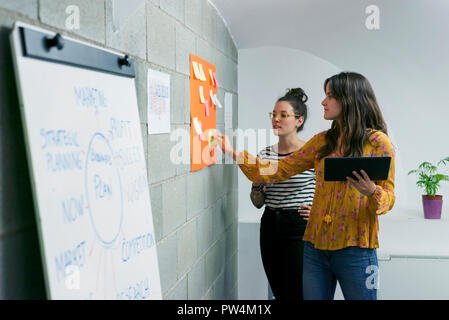 Female colleagues discussing over adhesive notes while standing in creative office Stock Photo