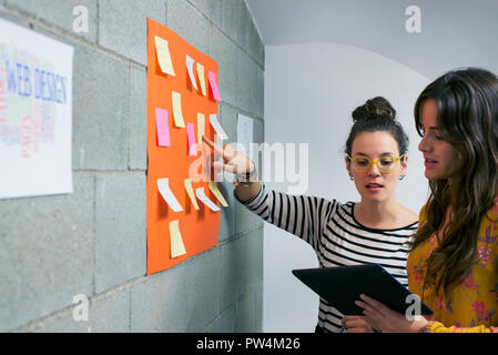 Female colleagues discussing adhesive notes over tablet computer while standing in creative office Stock Photo