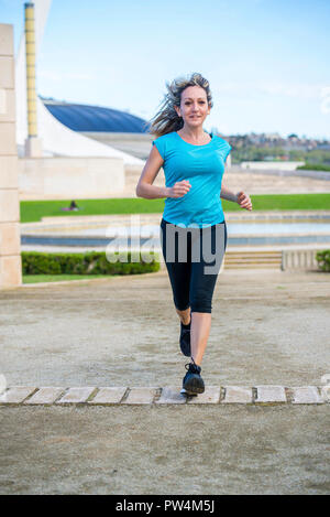 Portrait of confident female athlete running on footpath against sky at park Stock Photo