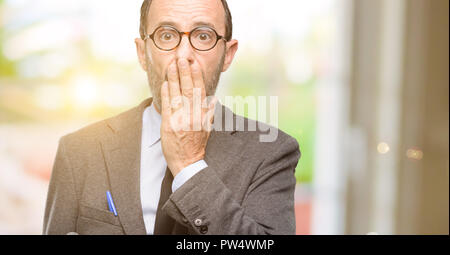 Teacher man using glasses covers mouth in shock, looks shy, expressing silence and mistake concepts, scared Stock Photo
