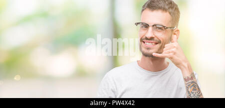 Young tattooed adult man smiling doing phone gesture with hand and fingers like talking on the telephone. Communicating concepts. Stock Photo