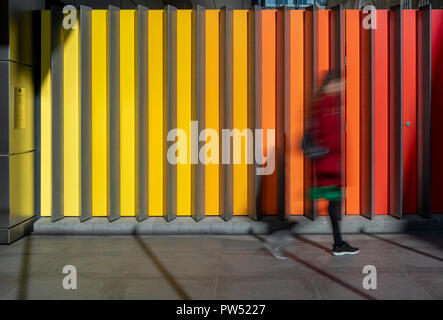 Blurred woman in a red coat walking in front of colourful striped background on Sun Street Passage, on the way to Liverpool Street Station in London. Stock Photo