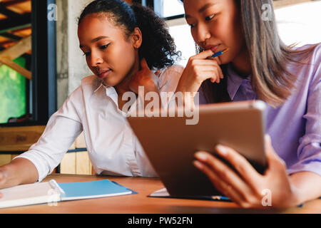 Close up of young businesswoman holding tablet pc. Two woman sitting at table in cafe. Stock Photo