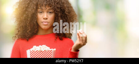 African american woman eating popcorn with a confident expression on smart face thinking serious Stock Photo